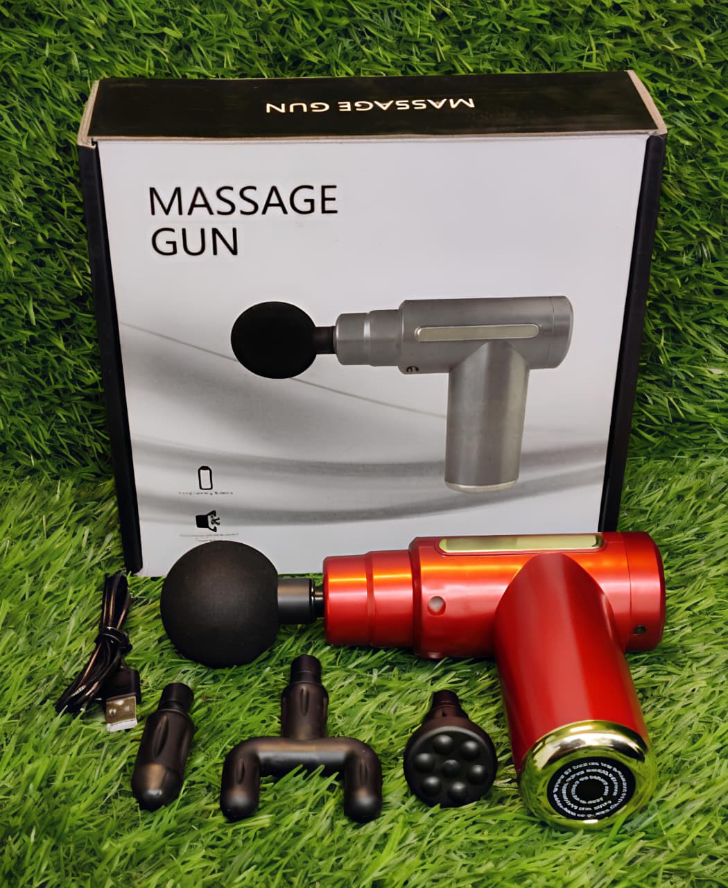 Massage gun with attachments on grass next to its packaging box.